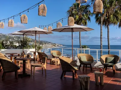 a patio with chairs tables and umbrellas and the ocean at Casa Loma Beach Hotel in Laguna Beach