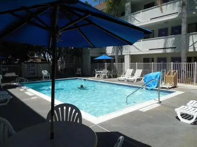 a pool with a blue umbrella and chairs and a person swimming at Motel 6-Chula Vista, CA - San Diego in Chula Vista