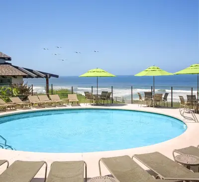a swimming pool with chairs and umbrellas and the ocean at WCH at Wave Crest Resort in Del Mar