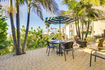 a patio with a table and chairs and palm trees at Tropical Oceanside Home with Deck, Walk to Beach in Oceanside