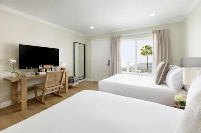 a hotel room with two beds and a desk and a television at Pacific Edge Hotel in Laguna Beach