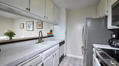 a kitchen with white cabinets and a stainless steel refrigerator at New Listing Ocean and Harbor View Cottage in Beach Resort in Oceanside