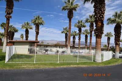 a fence in front of a building with palm trees at Stanlunds Inn and Suites in Borrego Springs