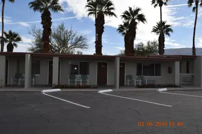 a building with palm trees and chairs in a parking lot at Stanlunds Inn and Suites in Borrego Springs