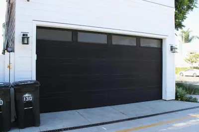 a black garage door on a house with two trash cans at Upper West Newport in Newport Beach